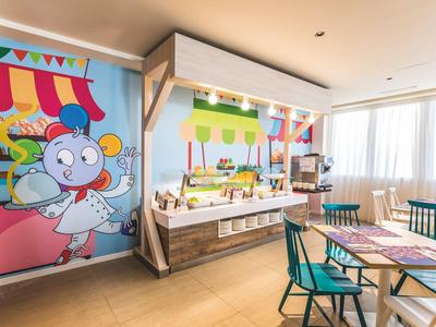 Bunter, heller Speiseraum mit Cartoon-Wandbild, Buffet und blau-grünen Stühlen an Holztischen.