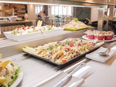 Buffet mit verschiedenen Salaten und Desserts auf großen weißen Tellern in heller Gaststätte.