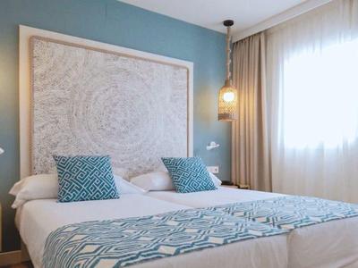 Modernes Schlafzimmer mit blauem Wandakzent, großem Bett, weißen Vorhängen und warmem Licht.