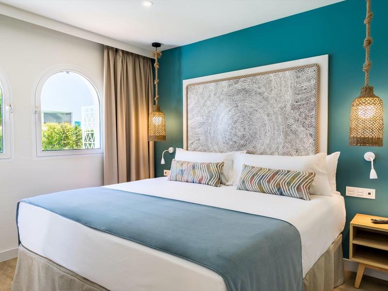 Modernes Schlafzimmer mit großem Bett, türkisfarbener Wand und runder Lampe aus Geflecht.