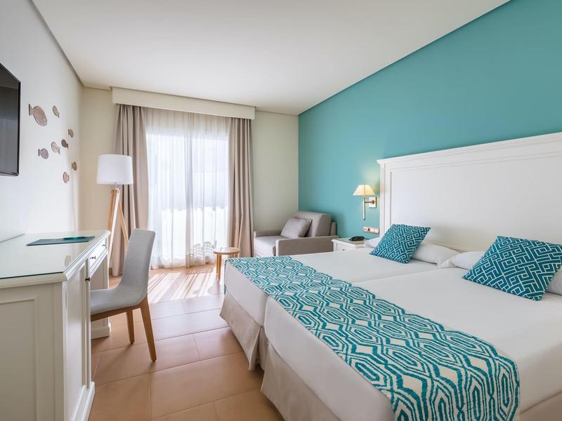 Modern eingerichtetes Hotelzimmer mit Doppelbett, weißem Mobiliar und hellblauen Akzenten.