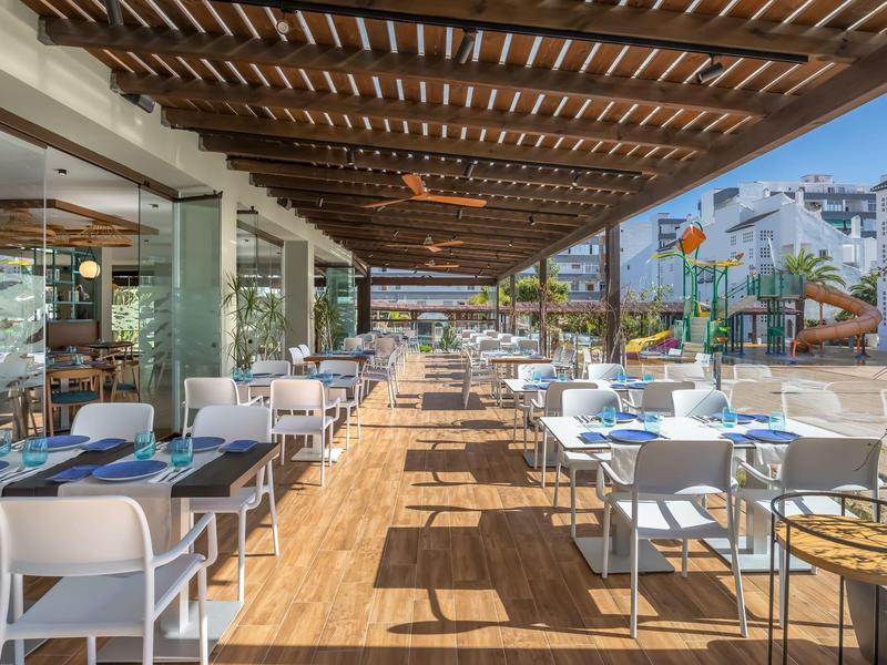 Freiluft-Terrasse mit weißem Mobiliar, Holzboden und Holzdach in modernem Restaurant.