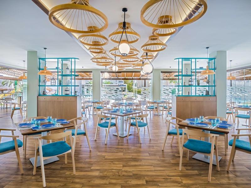 Modernes Restaurant mit Holzmöbeln, blauen Sitzpolstern und dekorativen Lampen an der Decke.