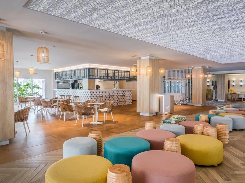 Moderner, heller Raum mit bunten Sitzhockern, Holzboden und großer Fensterfront für viel Tageslicht.