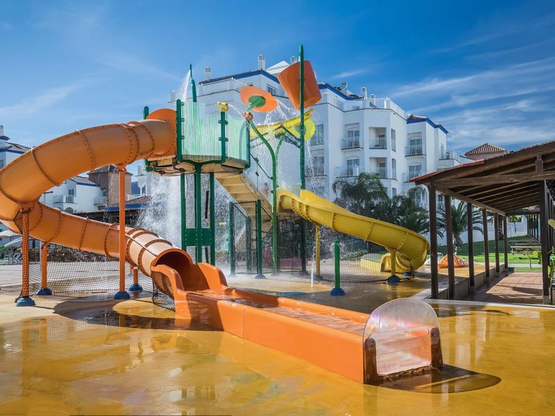 Ein großer Wasserpark mit bunten Rutschen und Rutschbahnen neben weißen Gebäuden und blauem Himmel.