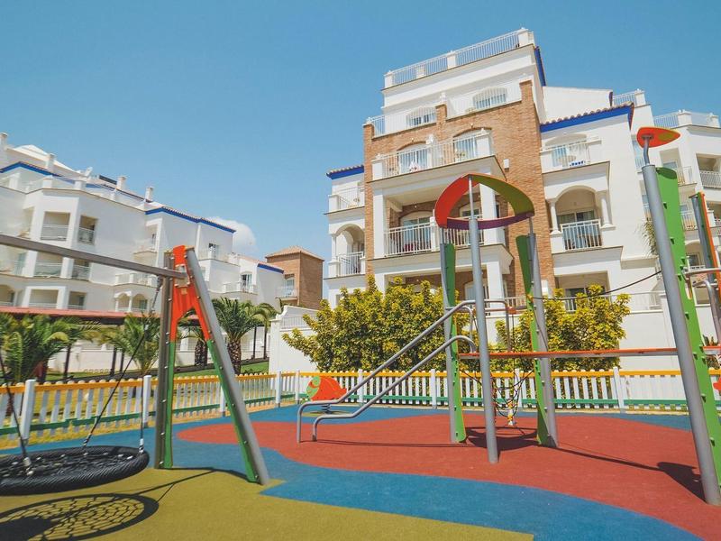 Großer bunter Spielplatz mit Schaukeln, Rutschen und Klettergerüsten vor mehrstöckigen Wohnhäusern.