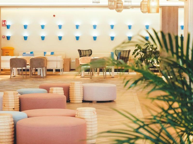 Heller, moderner Raum mit rosa Sitzmöbeln, Holzboden und Pflanzen im Vordergrund.