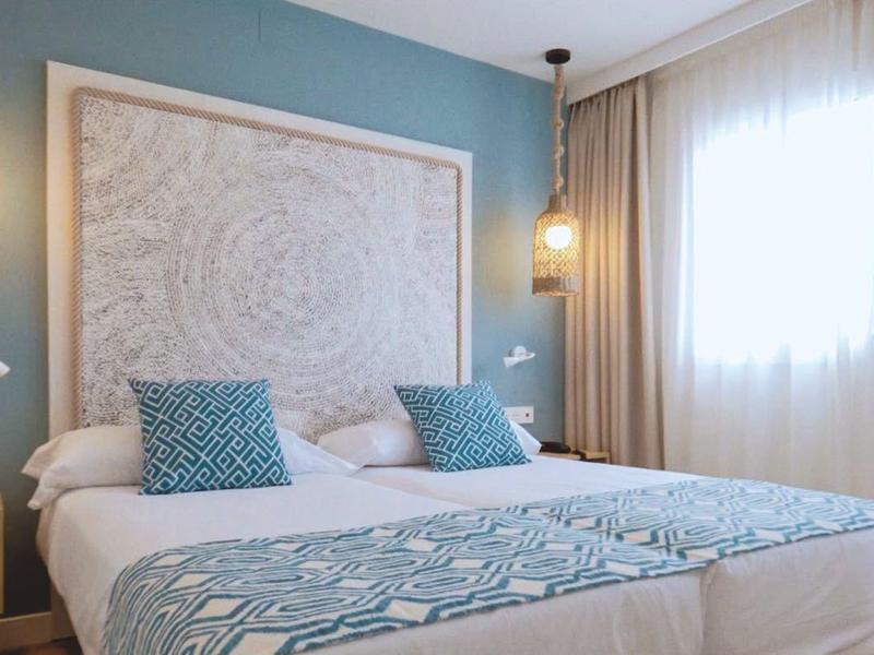 Modernes Schlafzimmer mit blauem Wandakzent, großem Bett, weißen Vorhängen und warmem Licht.