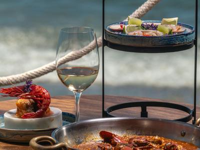 Gedeckter Tisch mit Meeresfrüchtegerichten und Weinglas am Strand.