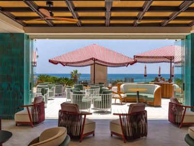 Moderner Außenbereich mit roten Sonnenschirmen, gepolsterten Sitzmöbeln und Blick aufs Meer.