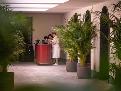 Rezeptionistin an einem Empfangstresen in einem hellen, modernen Hotelflur mit großen Topfpflanzen.