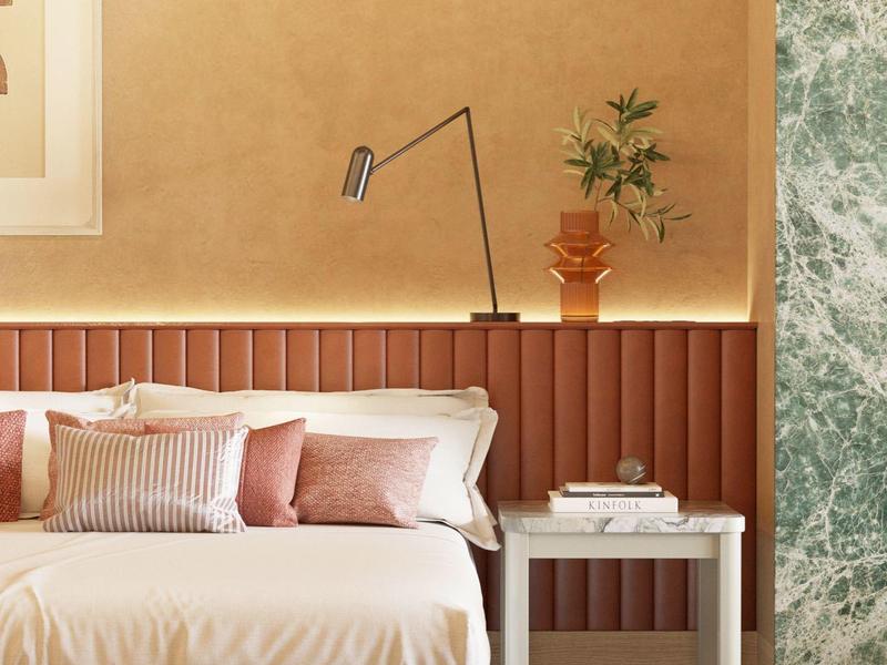 Gemütliches Schlafzimmer mit beigem Bett, rosa Kissen, Nachttisch und grüner Marmorwand.