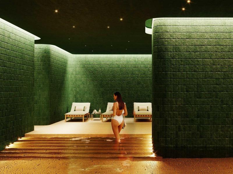 Frau in weißem Badeanzug läuft auf Holztreppe zu grünen, beleuchteten Wänden und Liegen.