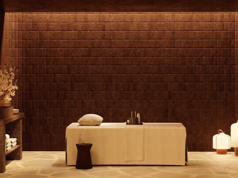 Modern eingerichteter Wellnessraum mit beleuchteter brauner Wand, Massagebank und gemütlicher Atmosphäre.