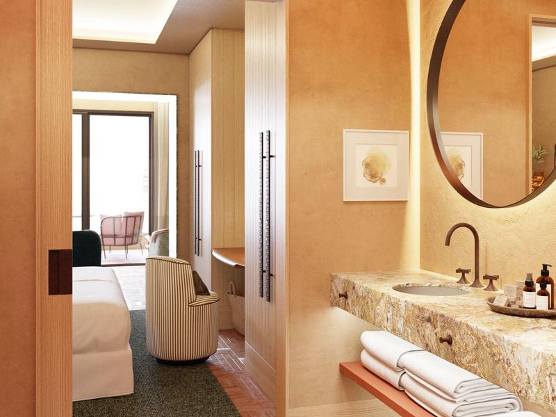 Modernes Badezimmer mit runden Spiegel, Waschbecken, Handtüchern und Blick ins Schlafzimmer.