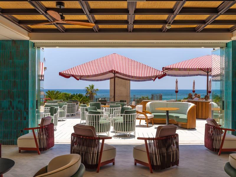 Moderner Außenbereich mit roten Sonnenschirmen, gepolsterten Sitzmöbeln und Blick aufs Meer.