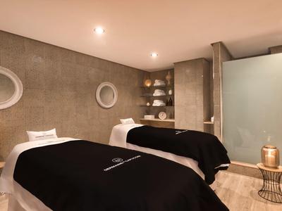 Moderner Wellnessraum mit zwei Massageliegen, grauen Wänden, runden Spiegeln und gedämpfter Beleuchtung.