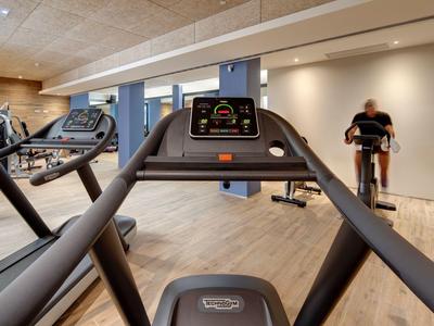 Salle de sport moderne avec tapis de course et sol en bois clair dans un hôtel.