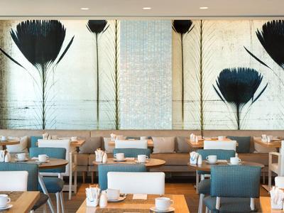 Restaurant moderne avec tables en bois, chaises bleues et art mural botanique.