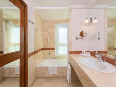 Hell beleuchtetes Badezimmer mit Badewanne, Waschbecken und großen Spiegeln