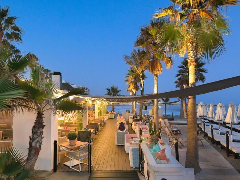 Restaurantterrasse am Strand mit beleuchteten Palmen und Abendstimmung.