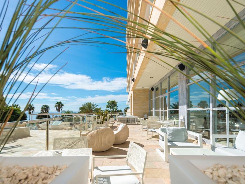 Terrasse mit modernen Sitzmöbeln und Blick auf einen Pool und Palmen unter blauem Himmel.