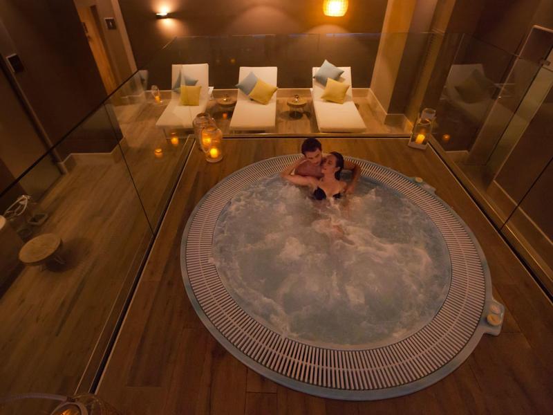 Paar entspannt in einem Whirlpool in einem luxuriösen Innenbereich mit Liegestühlen.