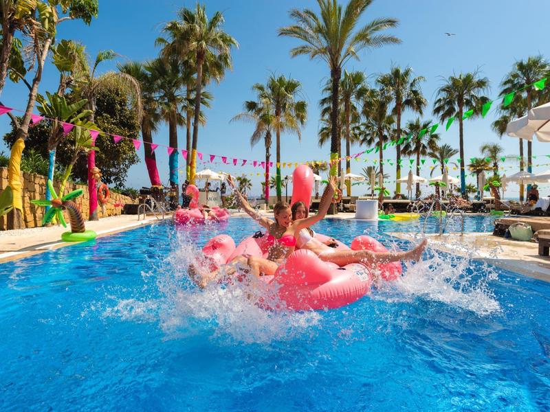 Person springt in einen Pool mit pinken Flamingo-Schwimmringen bei sonnigem Wetter