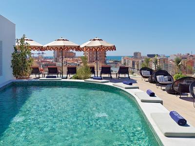 Ein klarer Pool mit blauer Wasseroberfläche, Sonnenschirme und Sitzmöbel auf einer Dachterrasse.