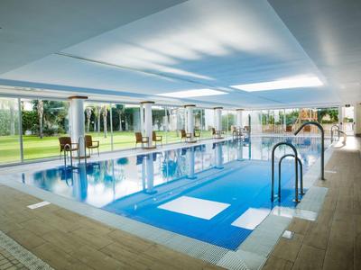 Hallenbad mit Glaswänden und Blick auf Garten mit Palmen