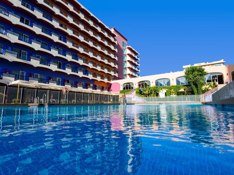 Moderner Hotelkomplex mit Außenpool und blauem Himmel im Hintergrund.