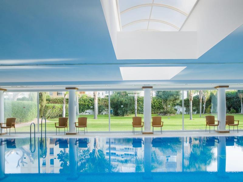 Innenpool mit Wasserflächen, Sonnenschirmen und Blick auf eine grüne Außenanlage