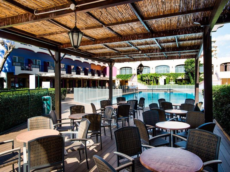 Überdachte Terrasse mit Tischen und Stühlen in einem Hotel neben dem Pool.