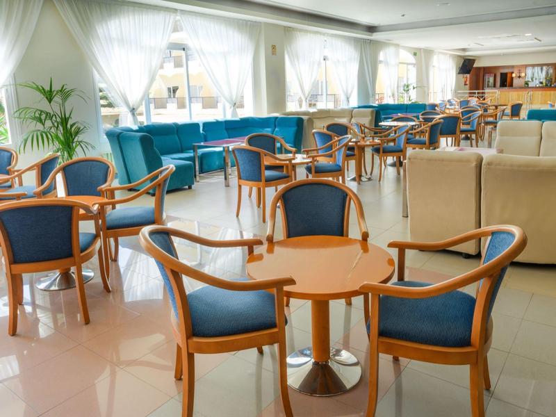 Heller Hotel-Sitzbereich mit Holzstühlen, blauen Polstern und Sofas neben großen Fenstern.