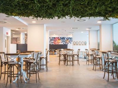 Moderner, heller Café-Raum mit Holzstühlen, Tischen und grüner Deckenpflanzen-Dekoration.