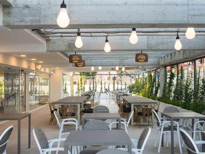 Helles, modernes Restaurant mit grauen Tischen, weißen Stühlen und hängenden Glühbirnen.