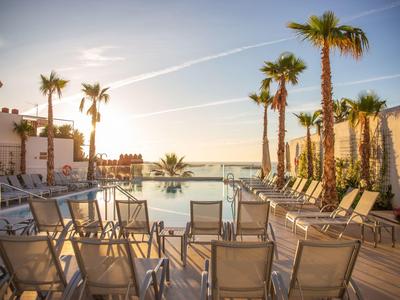 Sonnige Dachterrasse mit Pool, Liegestühlen und Palmen, Meerblick im Hintergrund bei klarem Himmel.