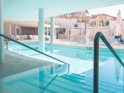 Moderner Innenpool mit klar blauer Wasserfläche, Treppen und Edelstahlgeländern. Helle Wände und große Fenster.