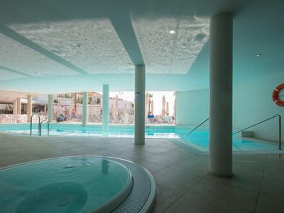 Innen beheiztes Schwimmbad mit Säulen, Whirlpool und großen Fenstern zum Außenbereich.