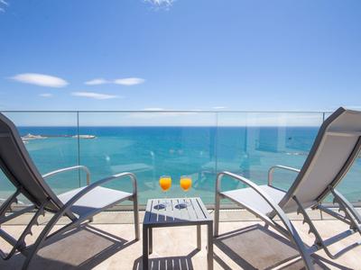 Dos tumbonas con una mesa y bebidas en un balcón con vistas al mar.