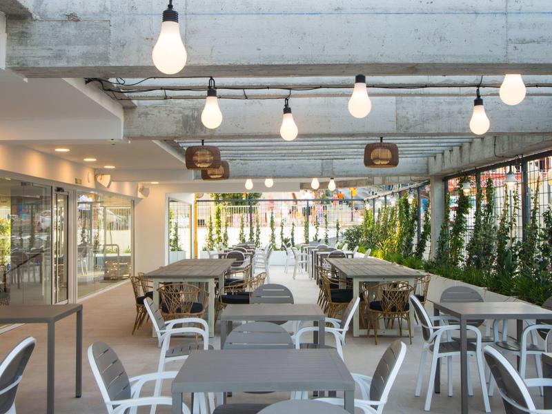 Helles, modernes Restaurant mit grauen Tischen, weißen Stühlen und hängenden Glühbirnen.