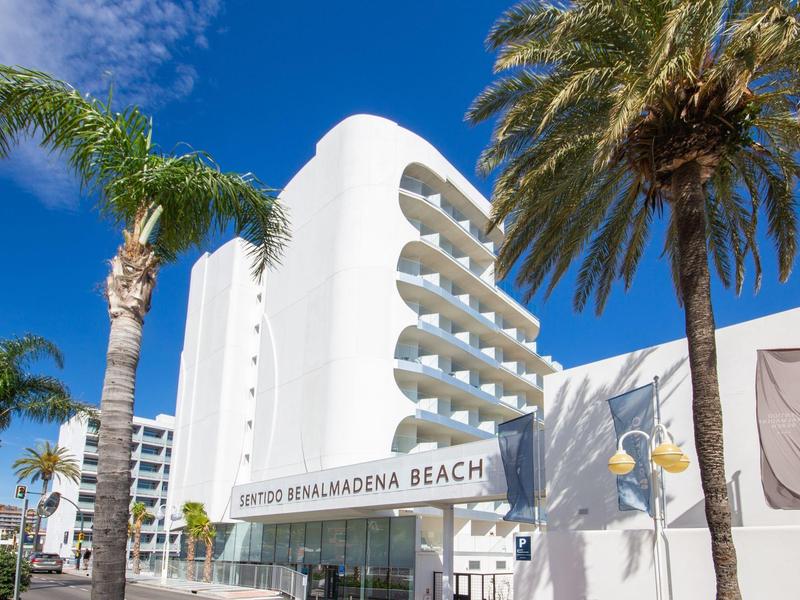 Weißes Hotelgebäude mit runden Balkonen, umgeben von hohen Palmen unter blauem Himmel.