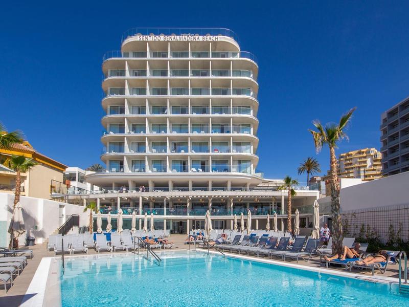 Modernes Hotel mit runden Balkonen, großem Pool und Liegestühlen unter blauem Himmel.