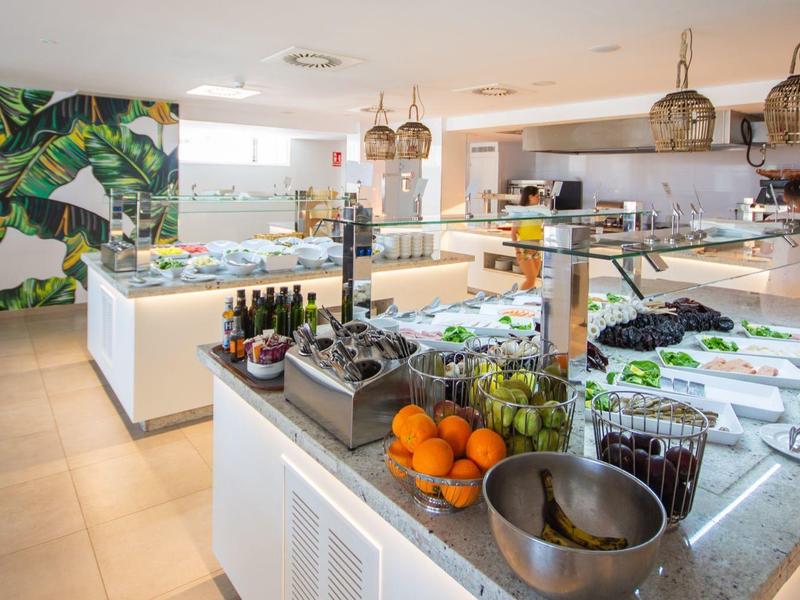 Moderne helle Buffetküche mit frischen Zutaten, weißen Möbeln und grüner Pflanzenwand.