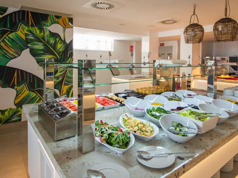 Buffet mit frischen Salaten und buntem Gemüse in modern gestalteter Küche mit Pflanzenmotiv-Wand.