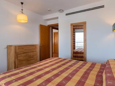 Schlafzimmer mit gestreiftem Bettbezug, Holzkommode, Spiegel und offenen Türen zu einem Flur.