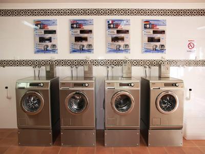 Vier wasmachines in een hotelwassruimte met instructies aan de muur er boven.