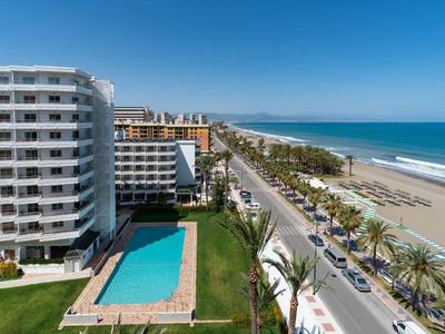 Moderne Hotels mit Pool neben Palmen gesäumter Straße und langem Sandstrand am blauen Meer.