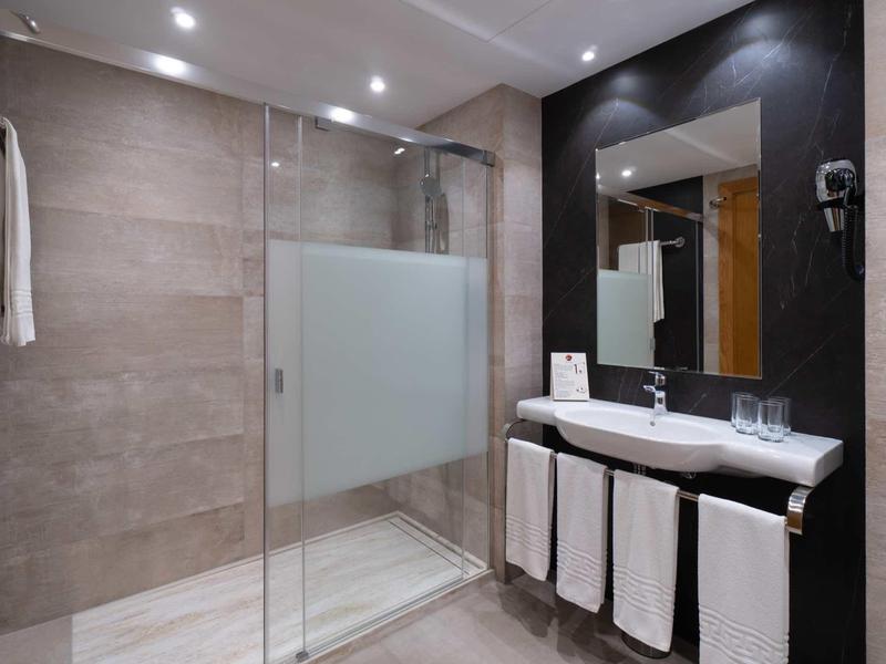 Modernes Badezimmer mit Glastür-Dusche, großem Spiegel und weißem Waschbecken mit Handtüchern.