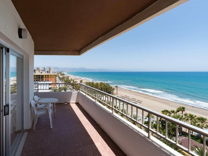 Balkon mit Stuhl und Tisch, Blick auf Strand, Meer und blauen Himmel bei sonnigem Wetter.